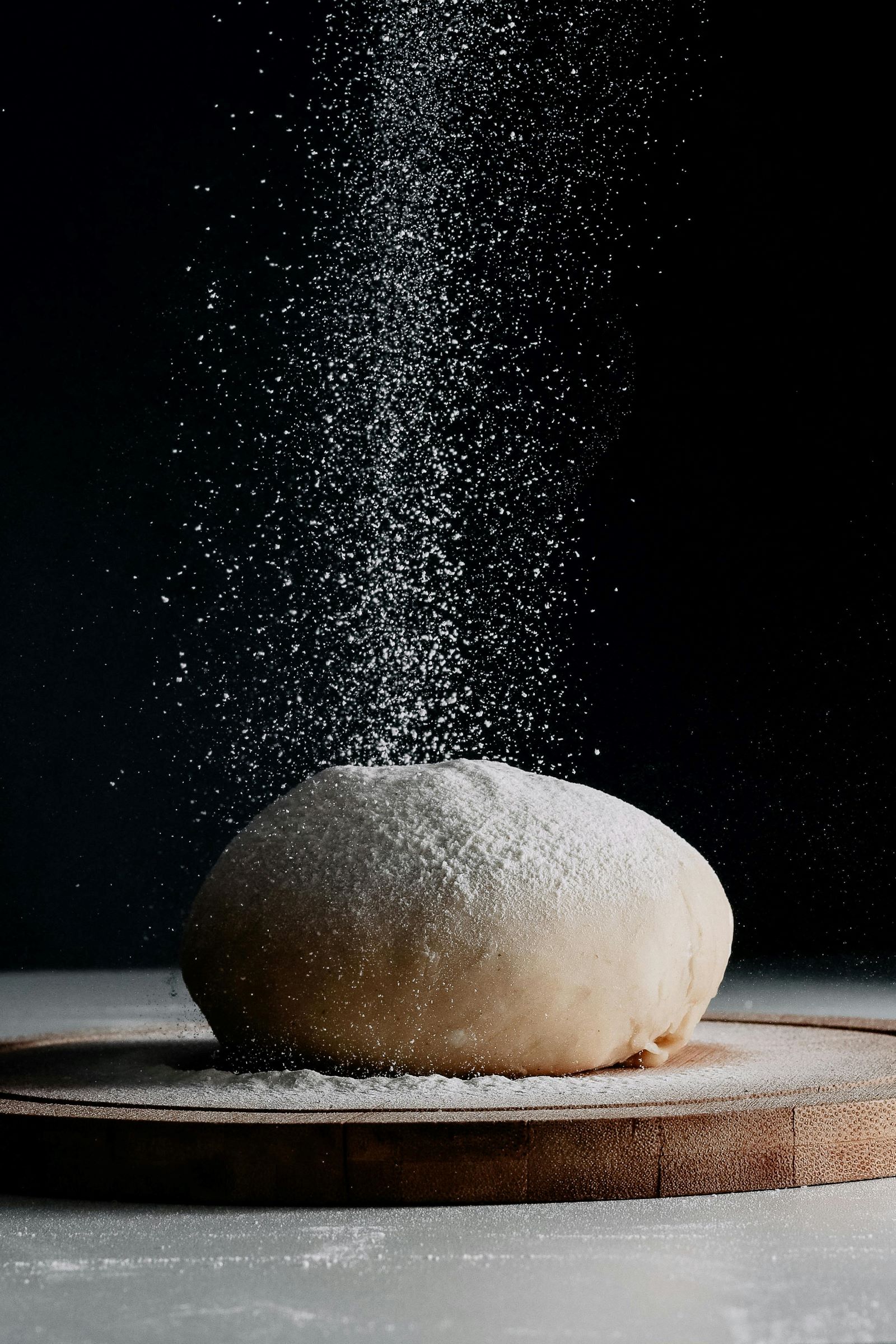A hand sprinkles flour over a dough ball, preparing it for baking delicious bread.