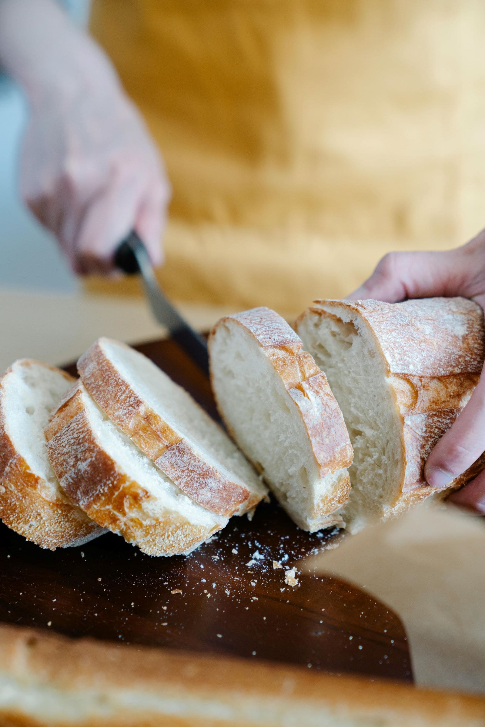 A person slices freshly baked bread on a wooden cutting board in a well-lit kitchen setting.