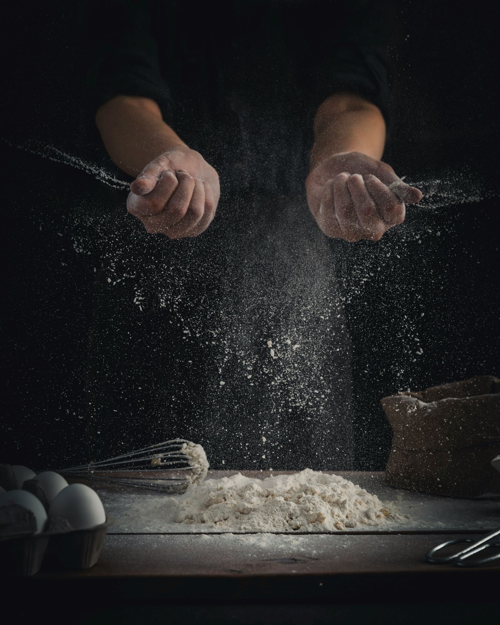 A person sprinkles flour on a table, preparing to bake delicious homemade bread with the best flour.