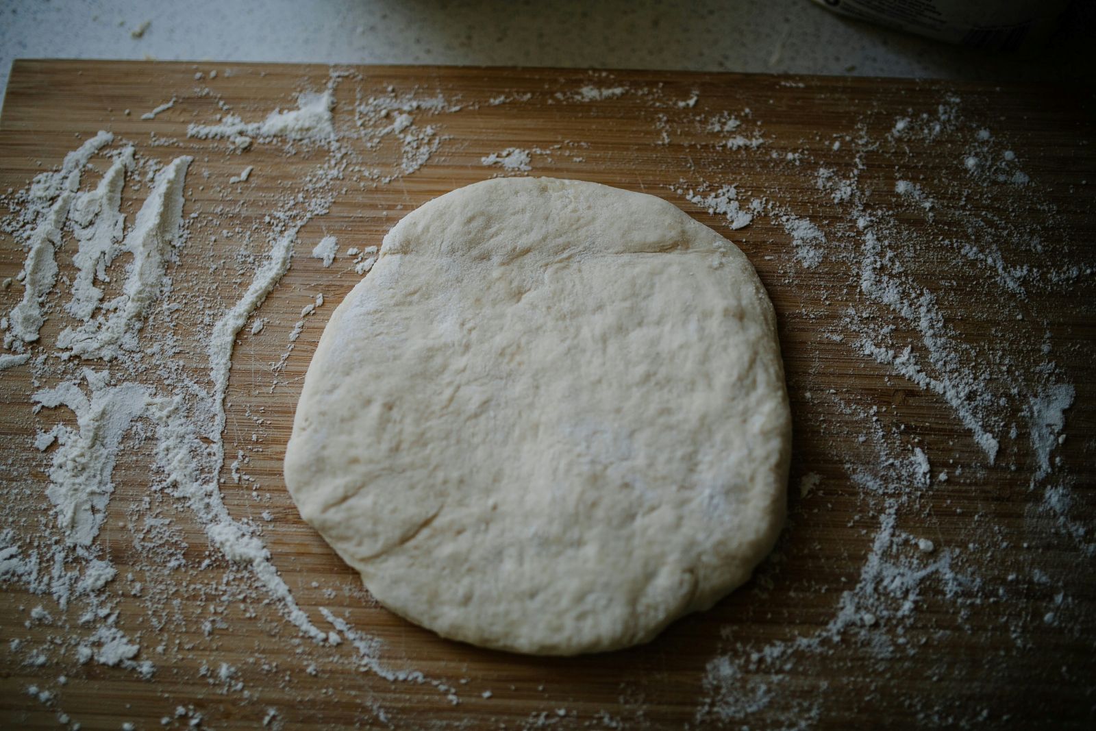 A ball of dough resting on a wooden cutting board, surrounded by a dusting of flour.