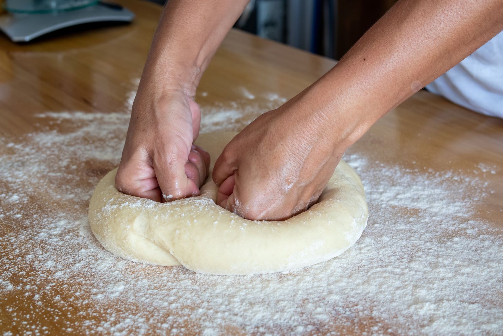 A person kneads pizza dough on a wooden table, demonstrating the technique for preparing the perfect crust.