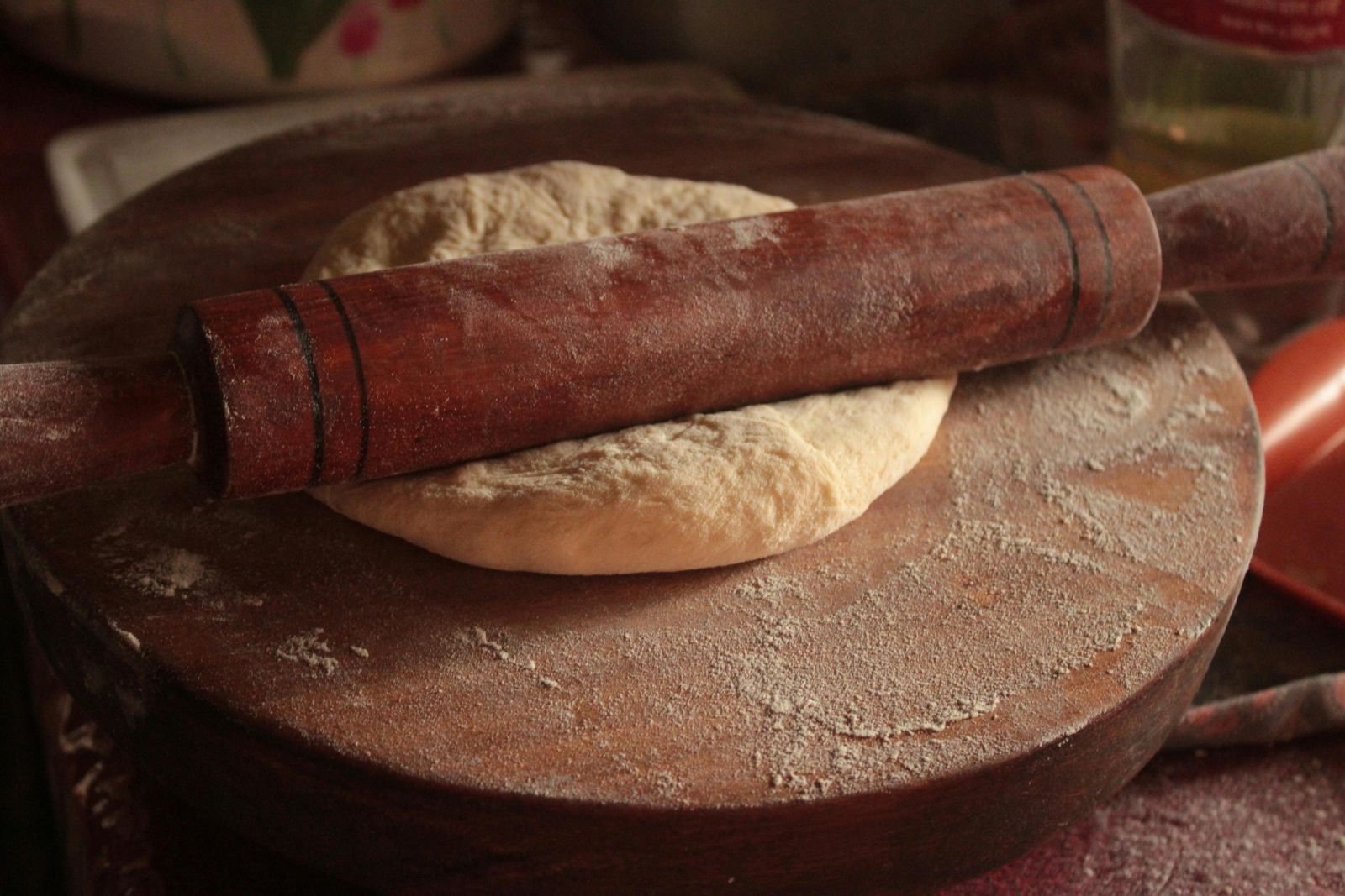 A dough ball resting on a wooden board, illustrating the process of kneading pizza dough.