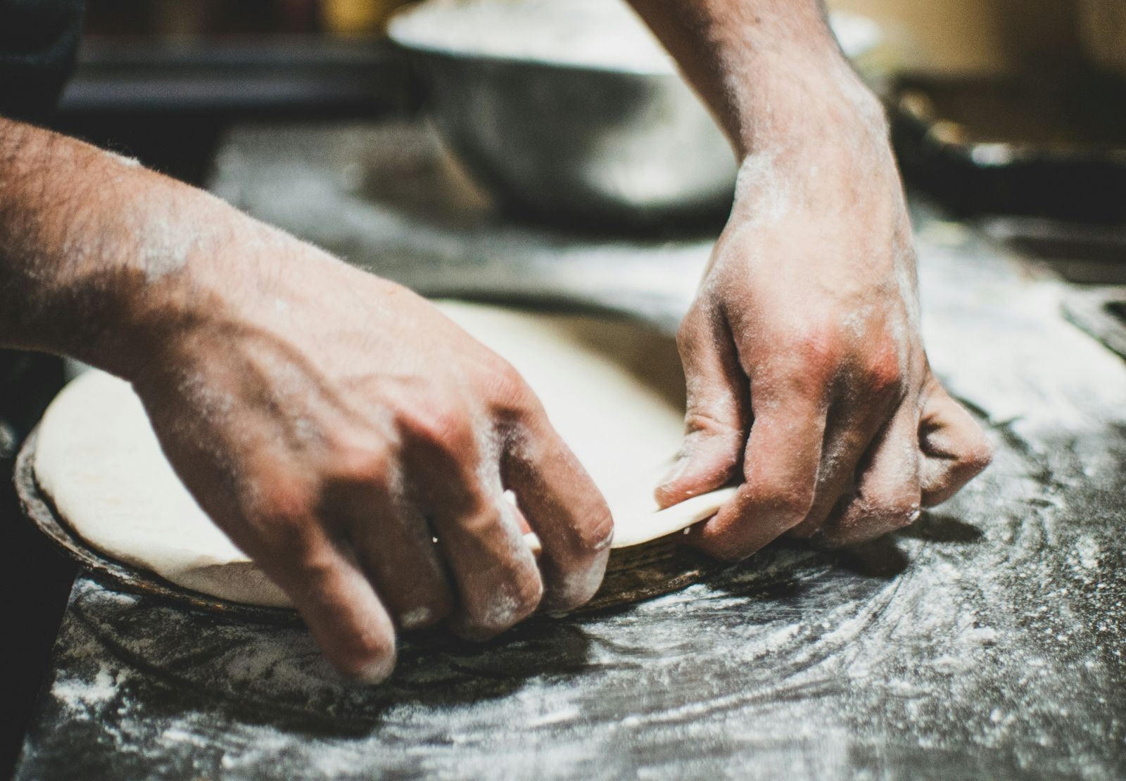 A person prepares a pizza on a countertop, showcasing fresh ingredients and dough in a kitchen setting.