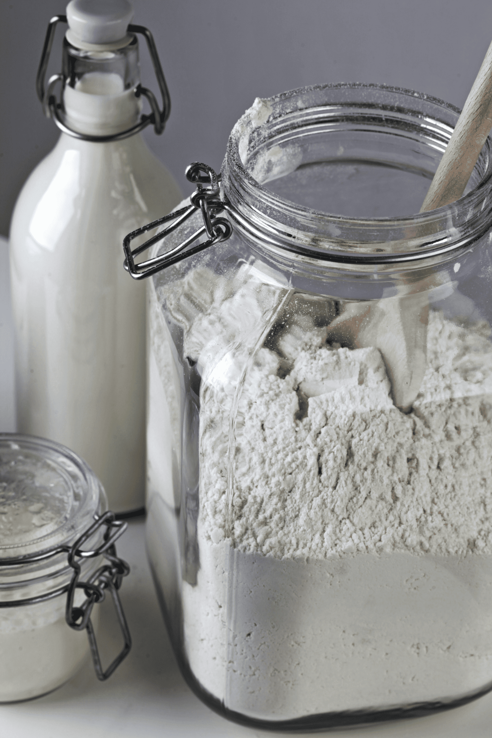 A jar of bread flour next to a jar of cake flour, with a jar of milk in the background, highlighting baking ingredients.