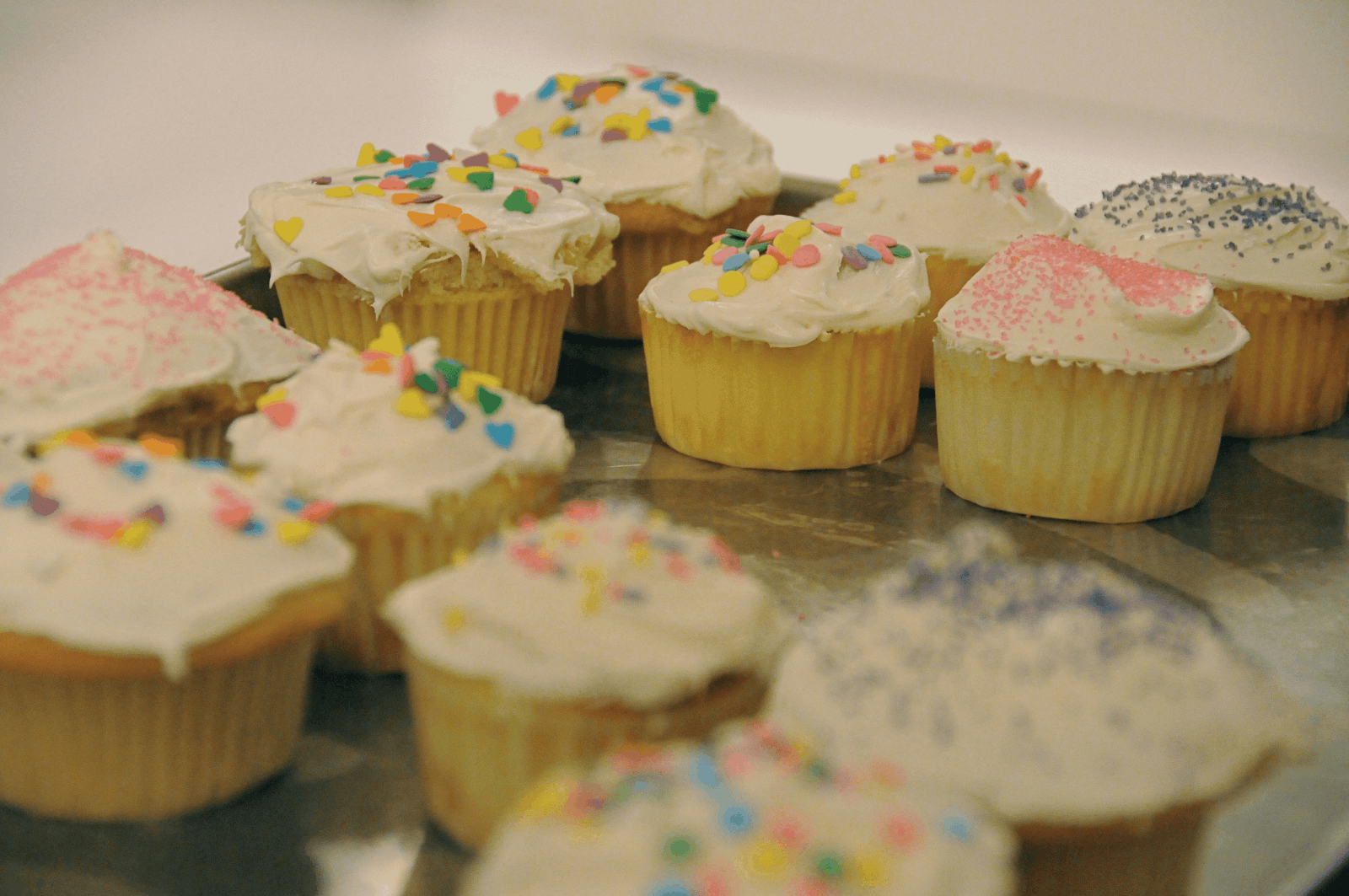 A tray filled with an assortment of colorful cupcakes, each topped with frosting and decorative sprinkles