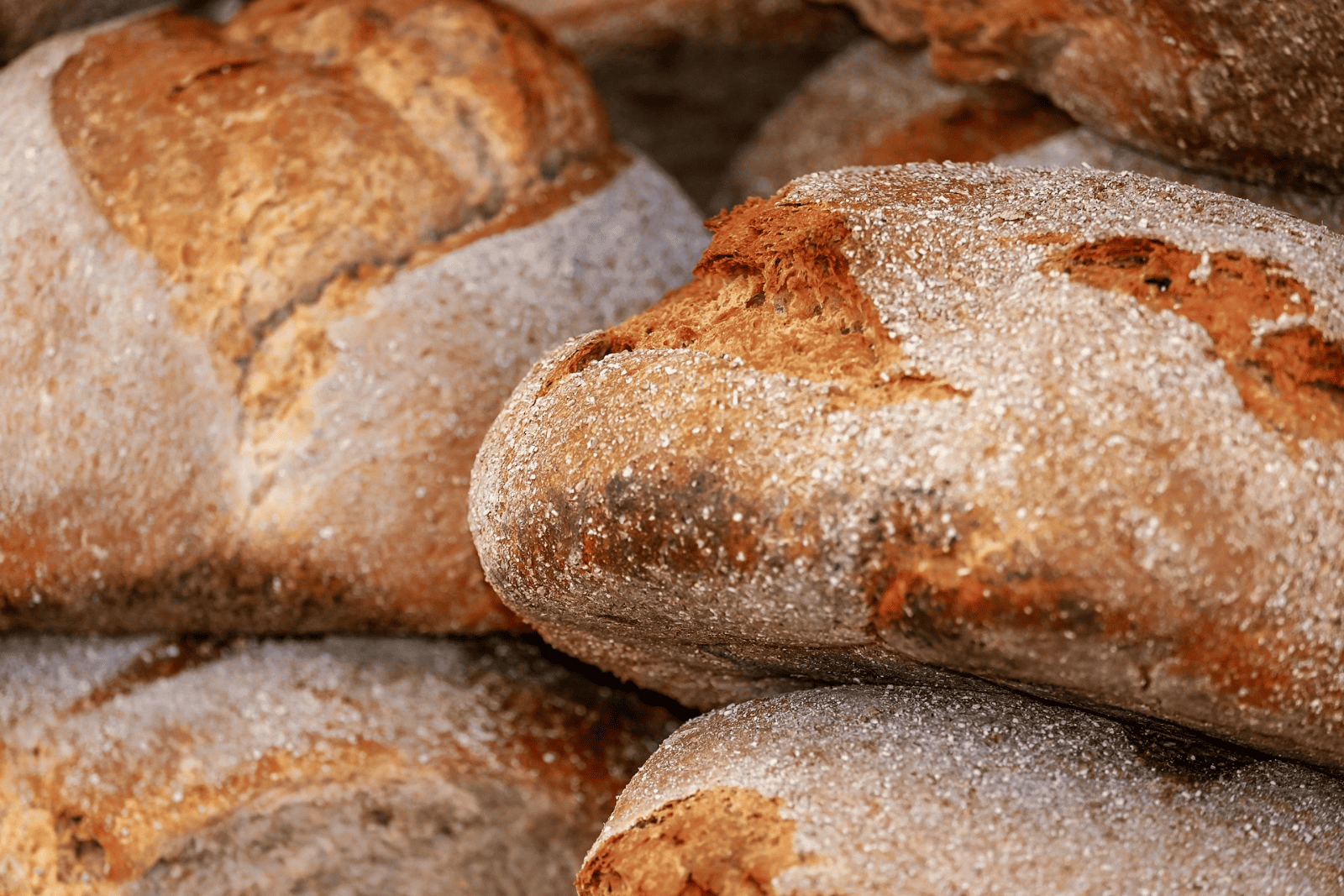 A variety of breads stacked on a wooden table, showcasing different shapes and textures.