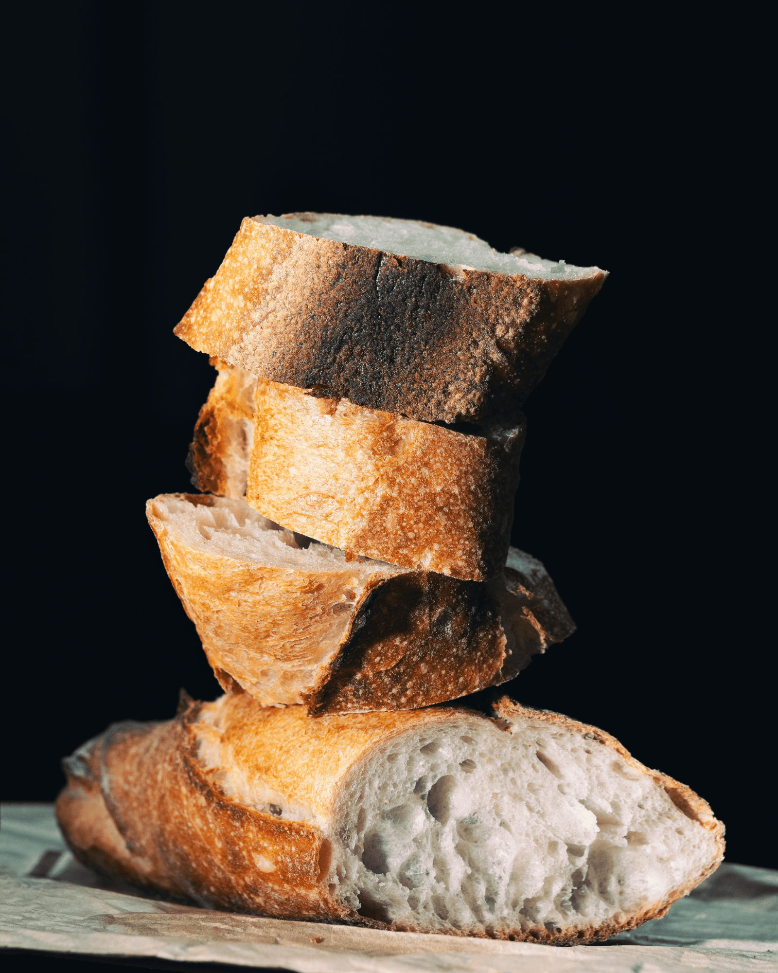 Stacked slices of rustic baguette, with a golden, crispy crust and soft interior, set against a dark background, evoke a sense of artisanal freshness